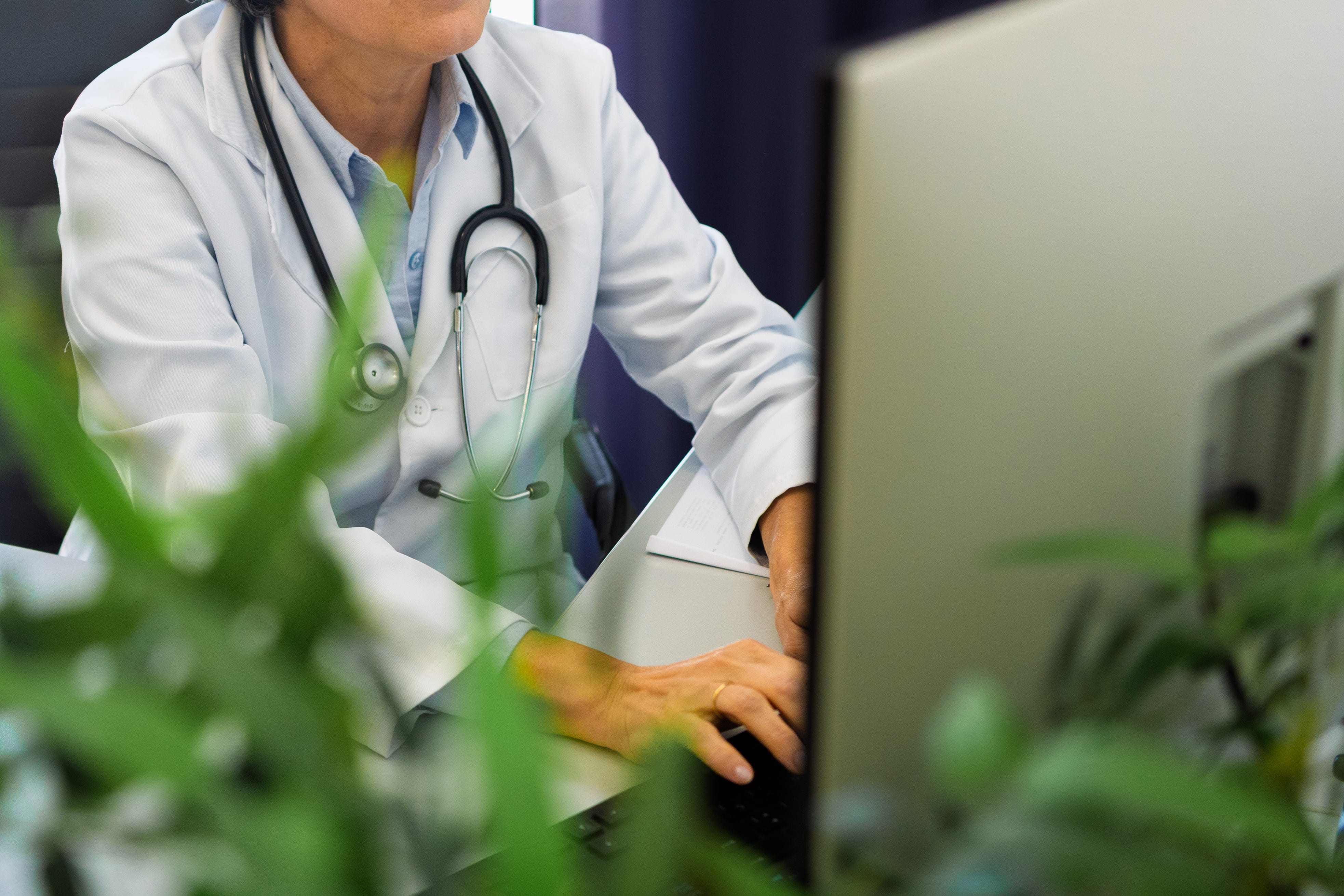Mature female physician working on computer, wearing white lab coat and stethoscope in medical workspace