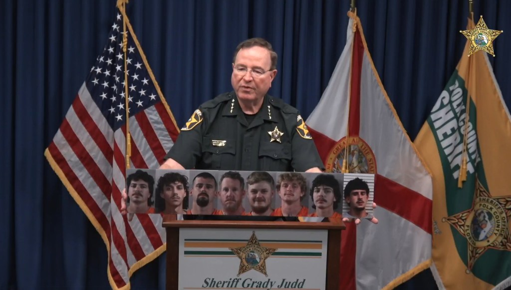 Sheriff Grady Judd holding mugshots of suspects.