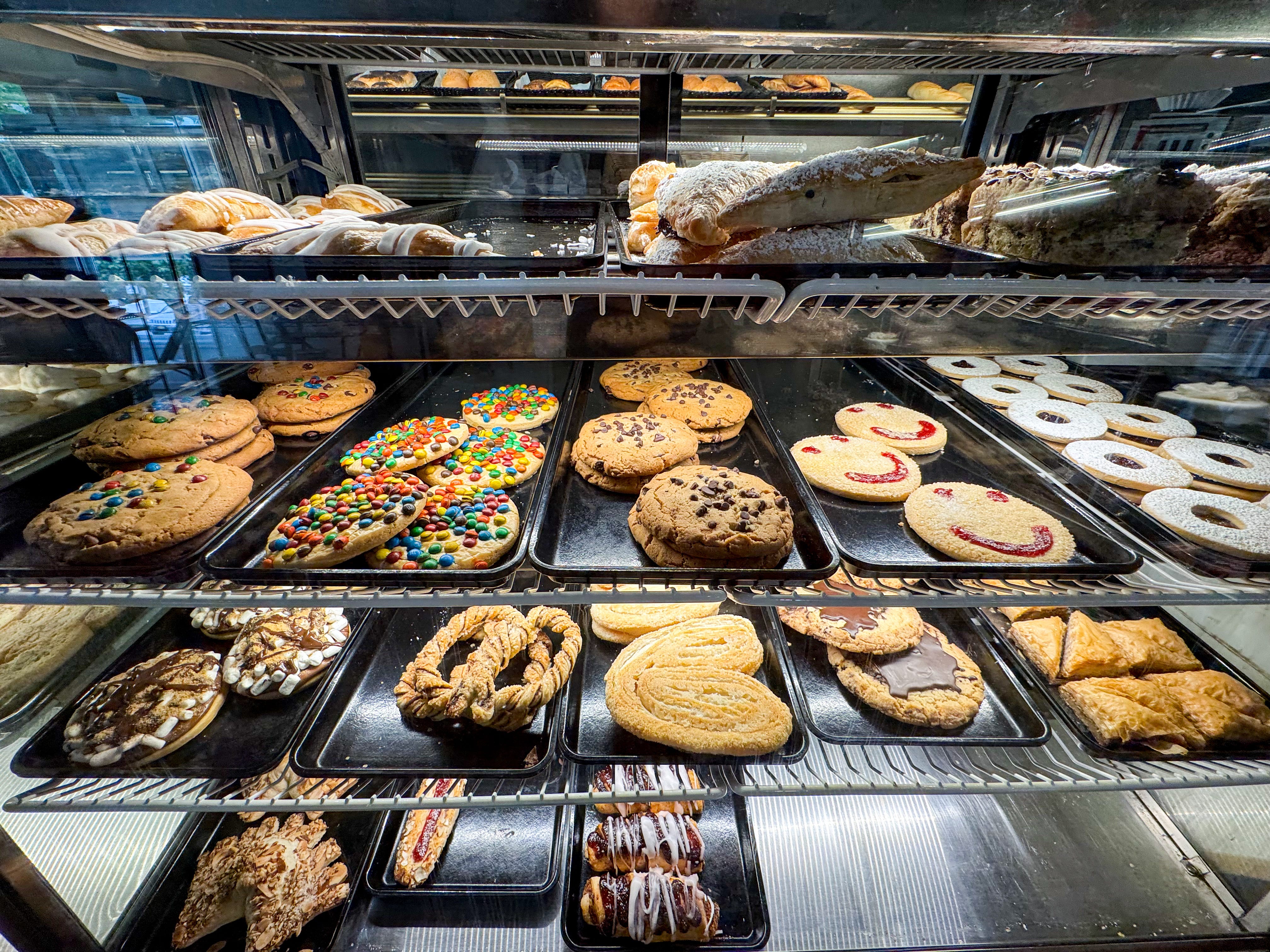 Four shelves of cookies and pastries on display in a bakery case.