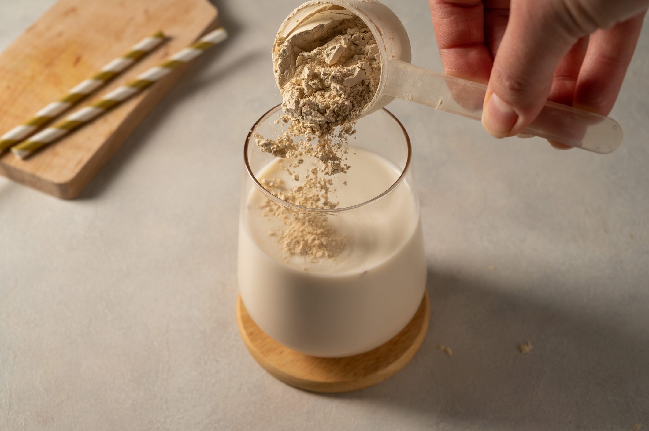 A hand adds a scoop of protein powder to milk.