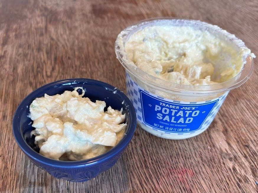 A small blue bowl of Trader Joe's potato salad next to the container.