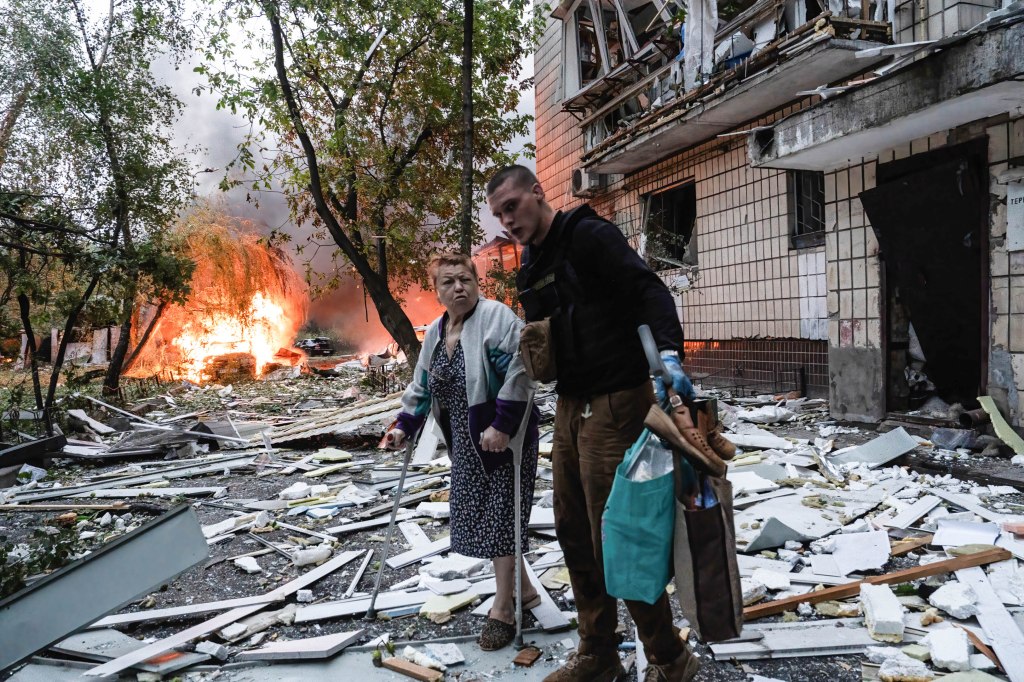An elderly woman using crutches is helped by a man to evacuate her damaged home following a missile strike in Kyiv, Ukraine.