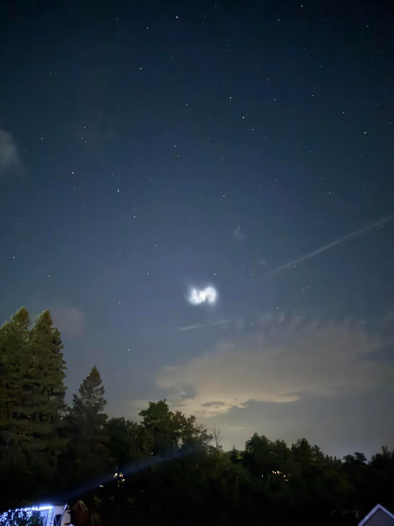 Night sky with bright light and swirling hues, possibly a rocket launch.