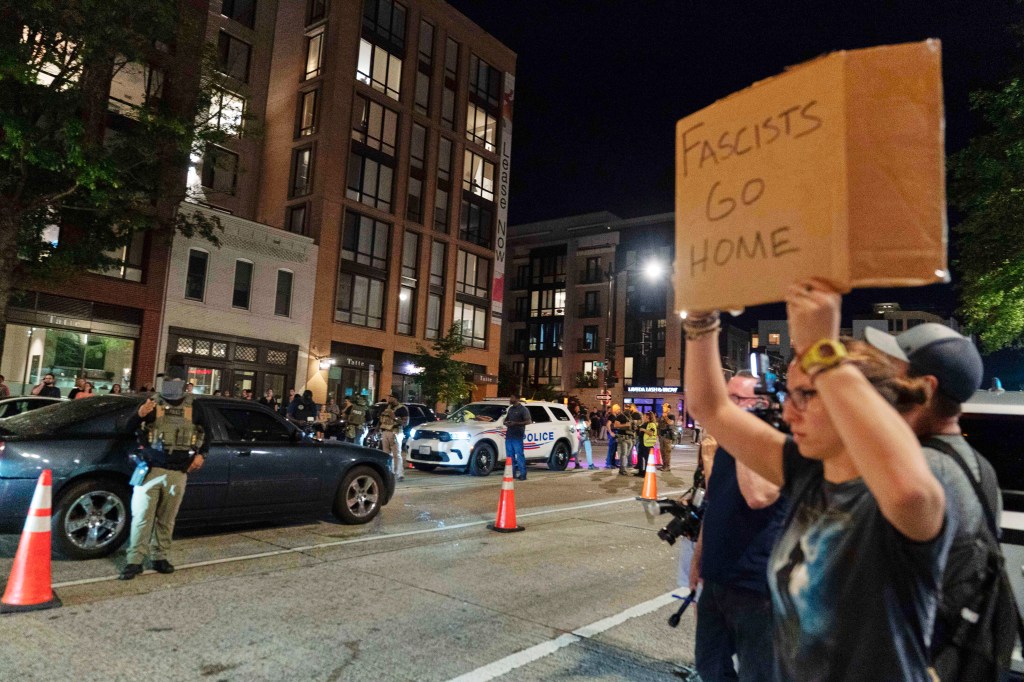 Protesters take to the streets holding signs near a traffic checkpoint run by Homeland Security agents and Washington Metropolitan Police officers along 14th Street in northwest Washington, DC, on Aug. 13, 2025.