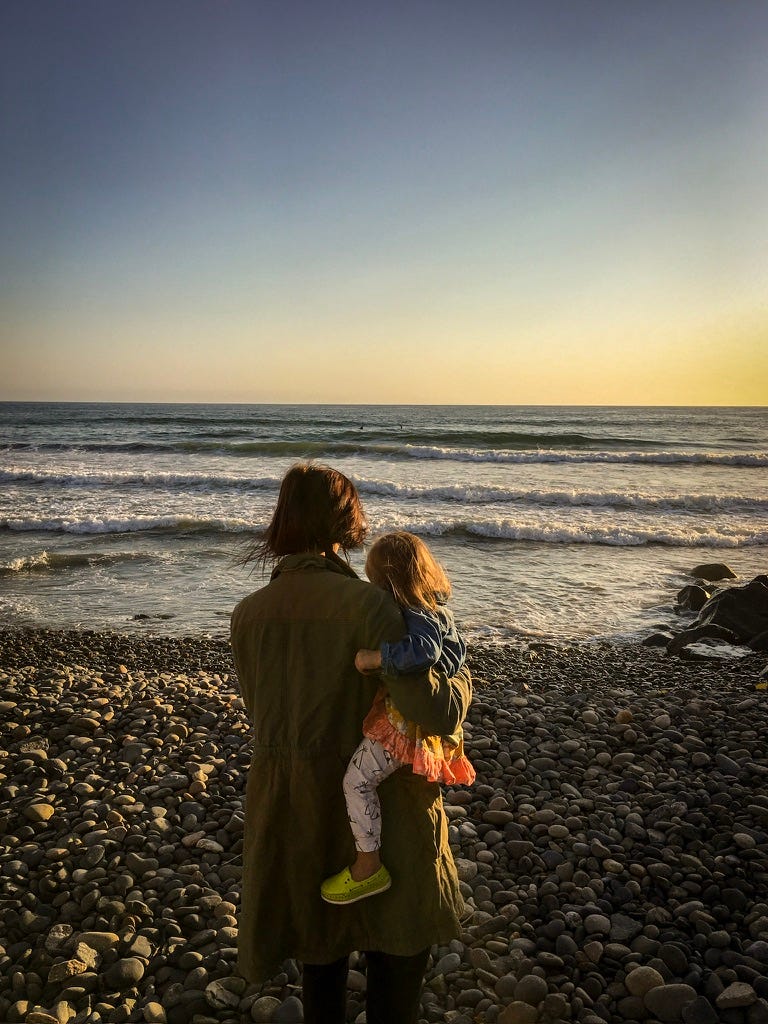 The author on a beach with her child looking out at the water at sunset.