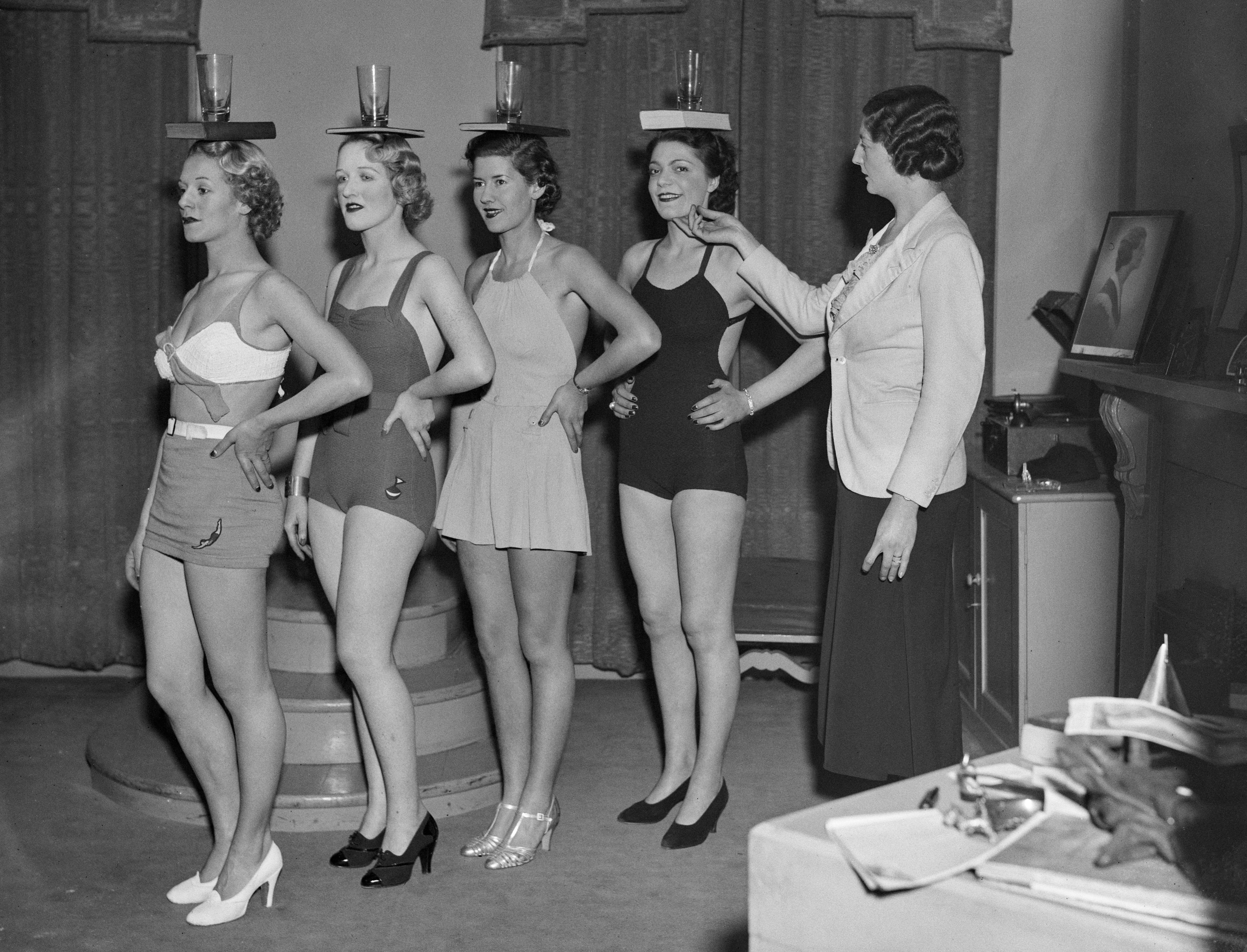 Sylvia Lucie Golledge (right) instructs pupils in the art of correct posture by balancing a glass and book on their heads at her modelling agency and finishing school in Old Cavendish Street, London, 25th November 1936.