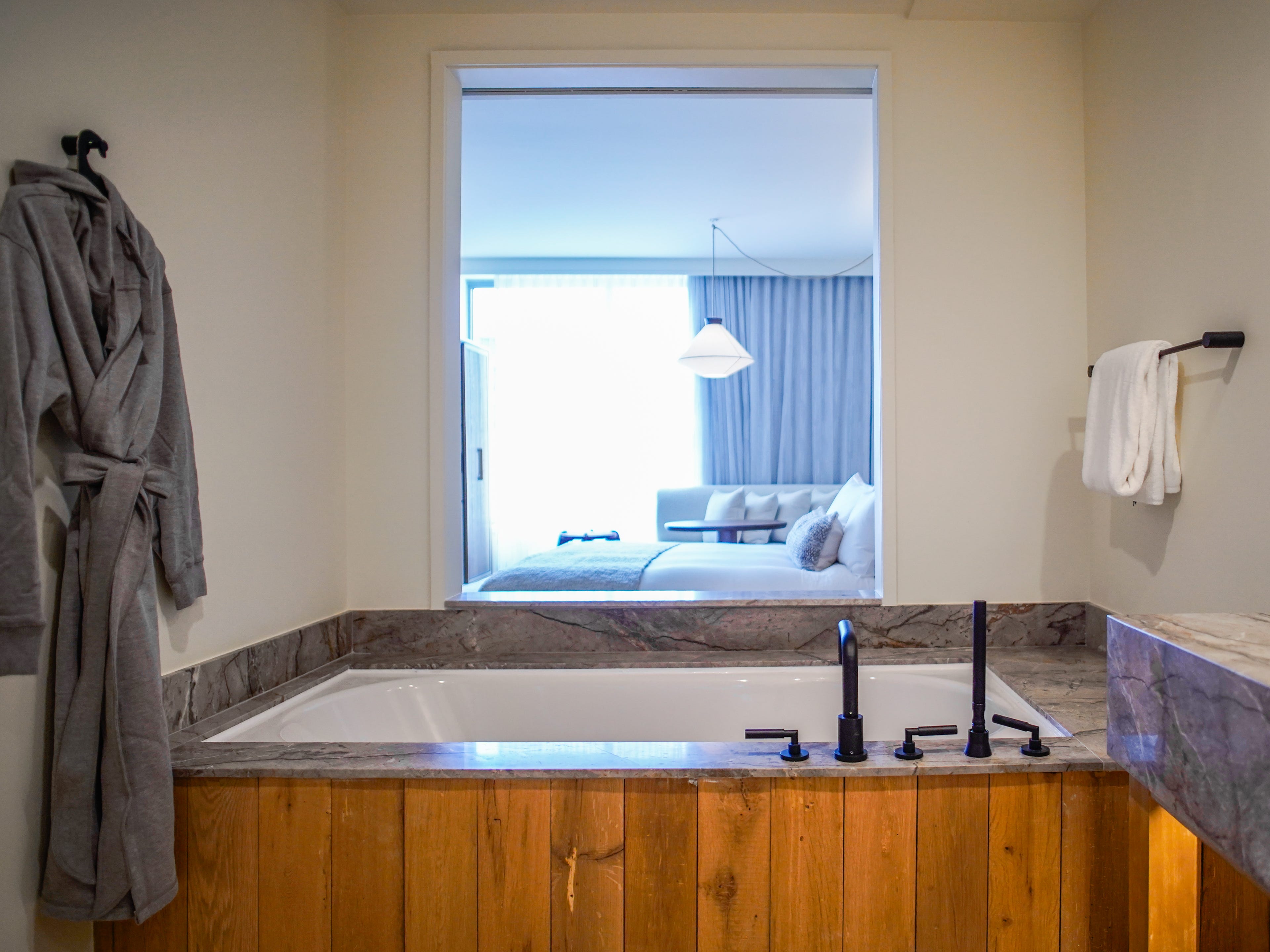 A bathtub at 1 Hotel Seattle with a robe on the left and a window to the bedroom in the center