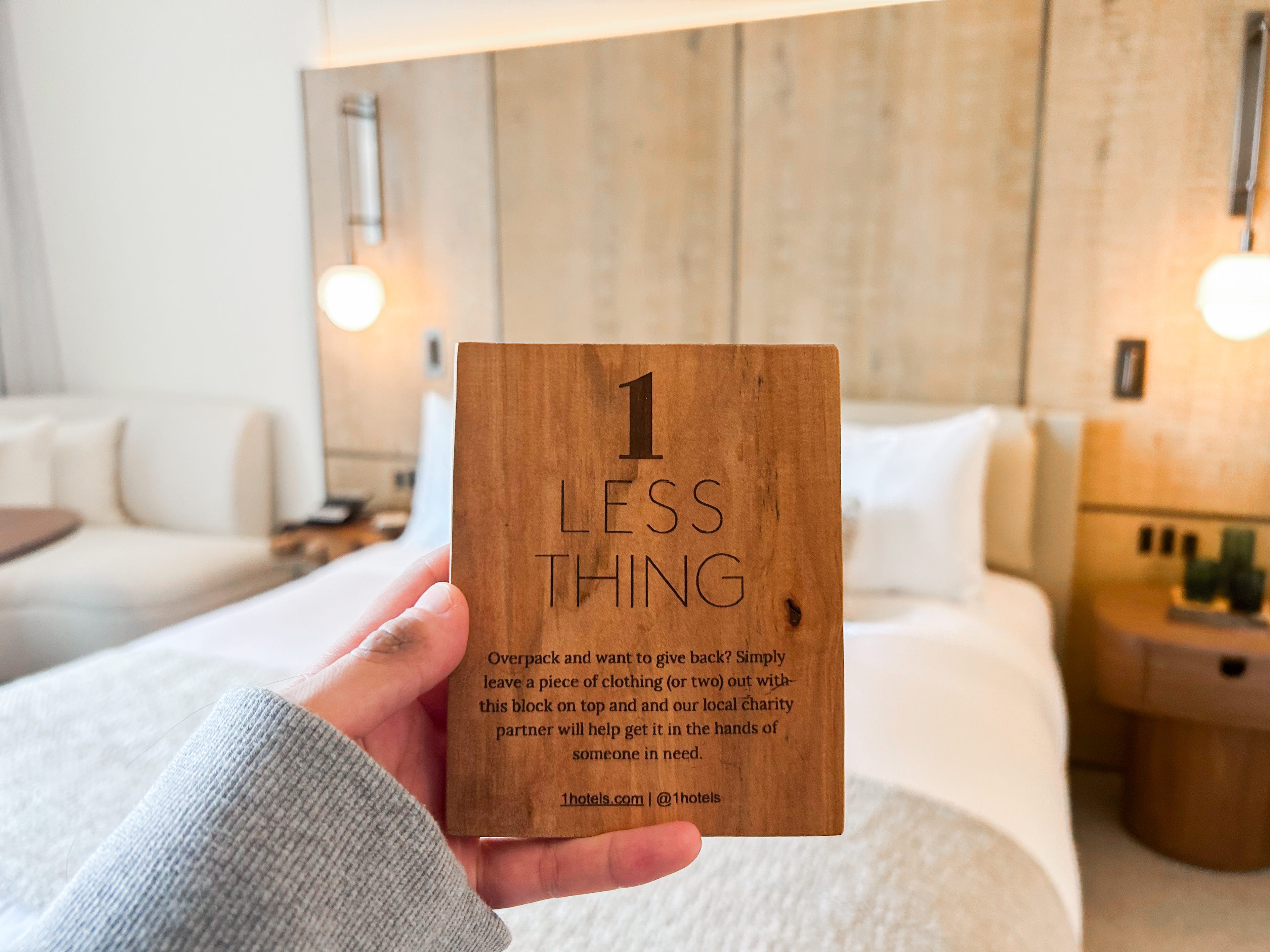 A hand holding a wood plaque in front of a bed