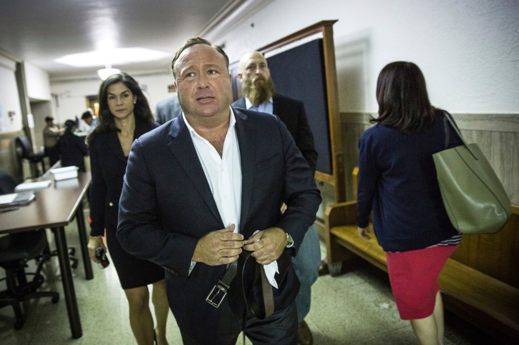 Alex Jones walking in a courthouse hallway.