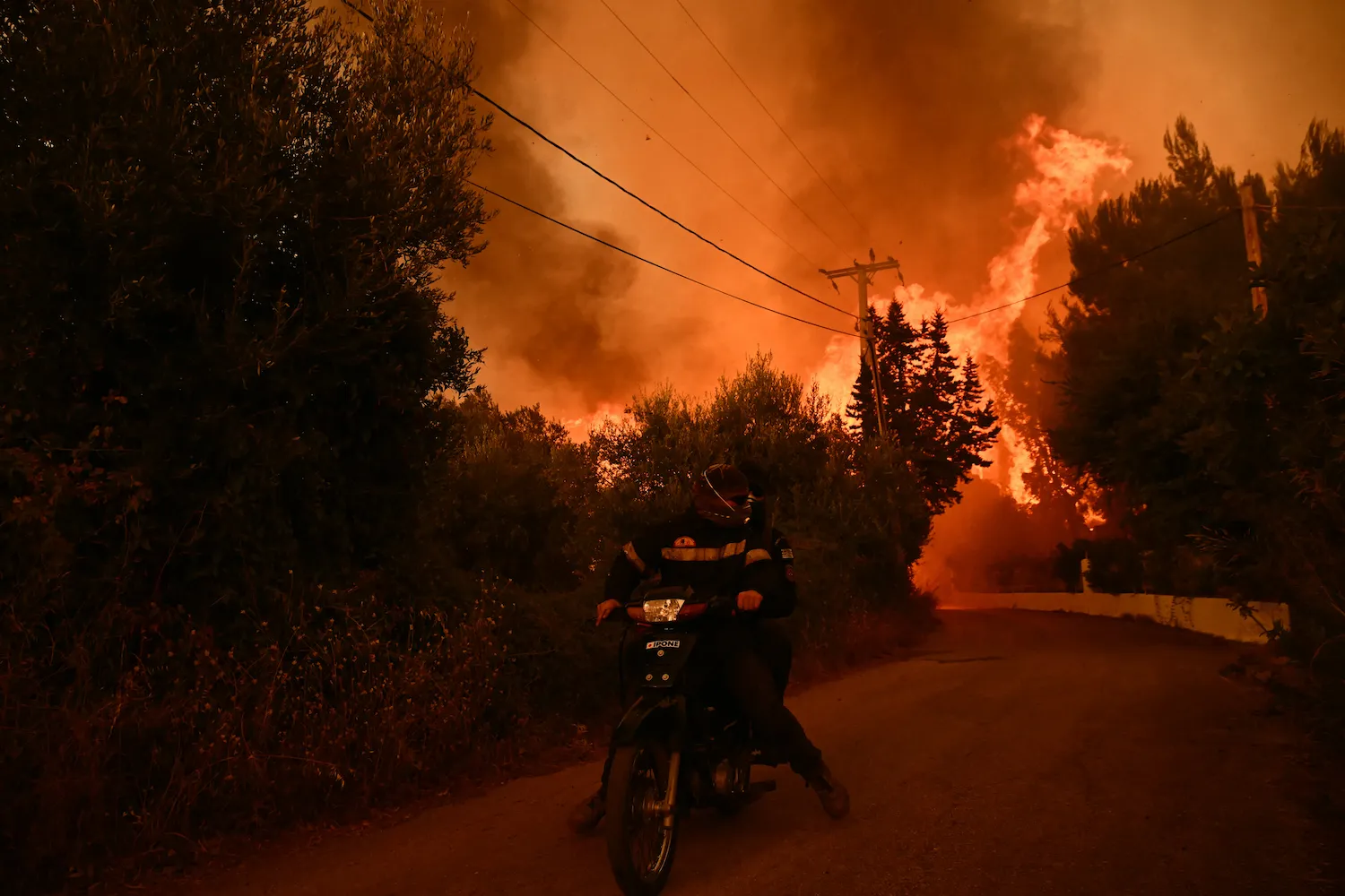 Firefighters leave an area on a scooter as flames approach during a wildfire near the city of Patras, western Greece, on Aug. 13. The country has battled to contain more than 20 wildfires including one menacing its third-largest city, Patras, as a heat wave stoked blazes and forced the evacuation of thousands in southern Europe. 