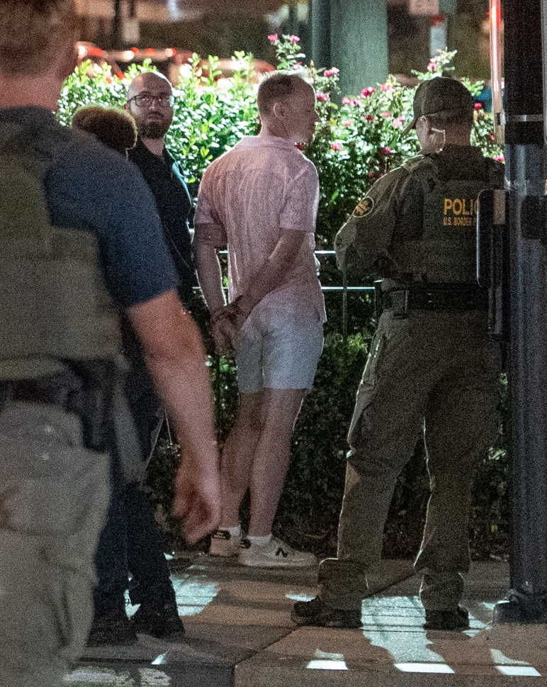 A man in handcuffs being questioned by law enforcement officers.