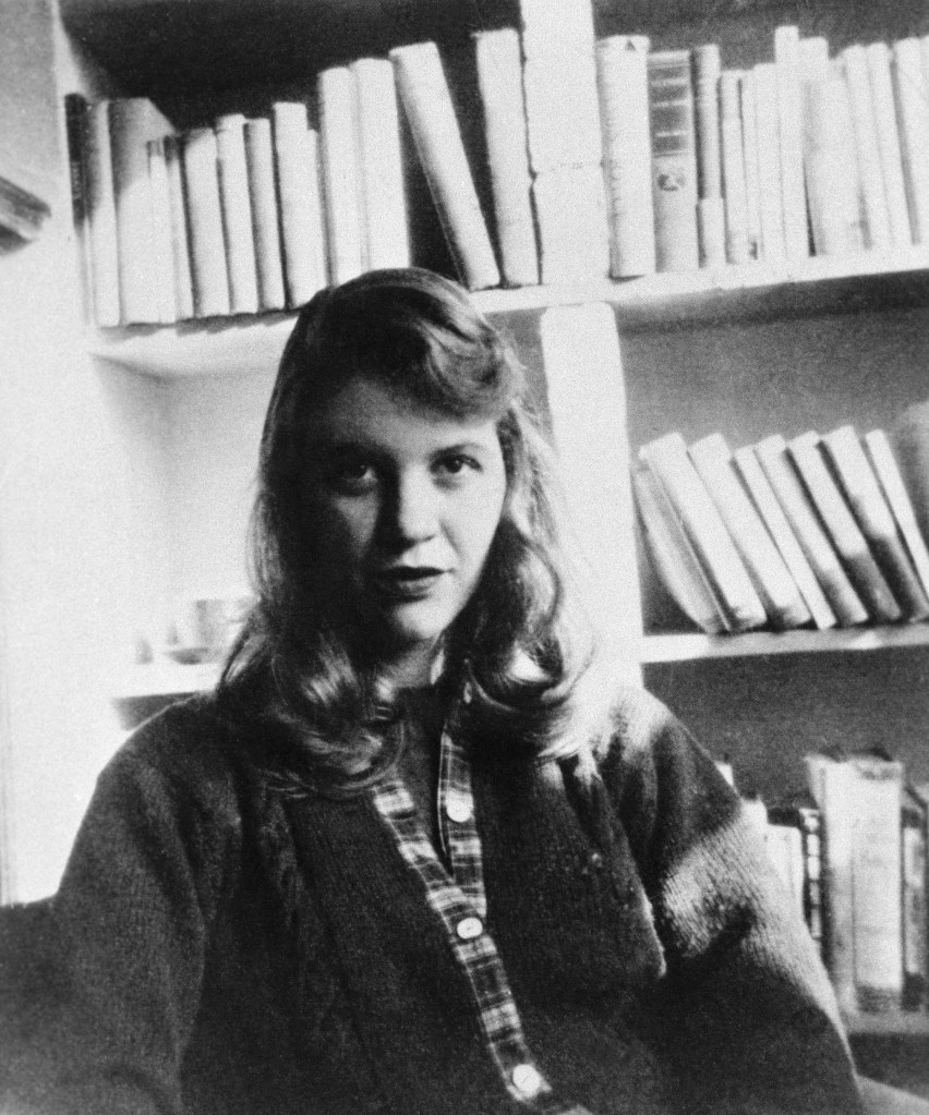 Black and white photo of Sylvia Plath seated in front of a bookshelf.