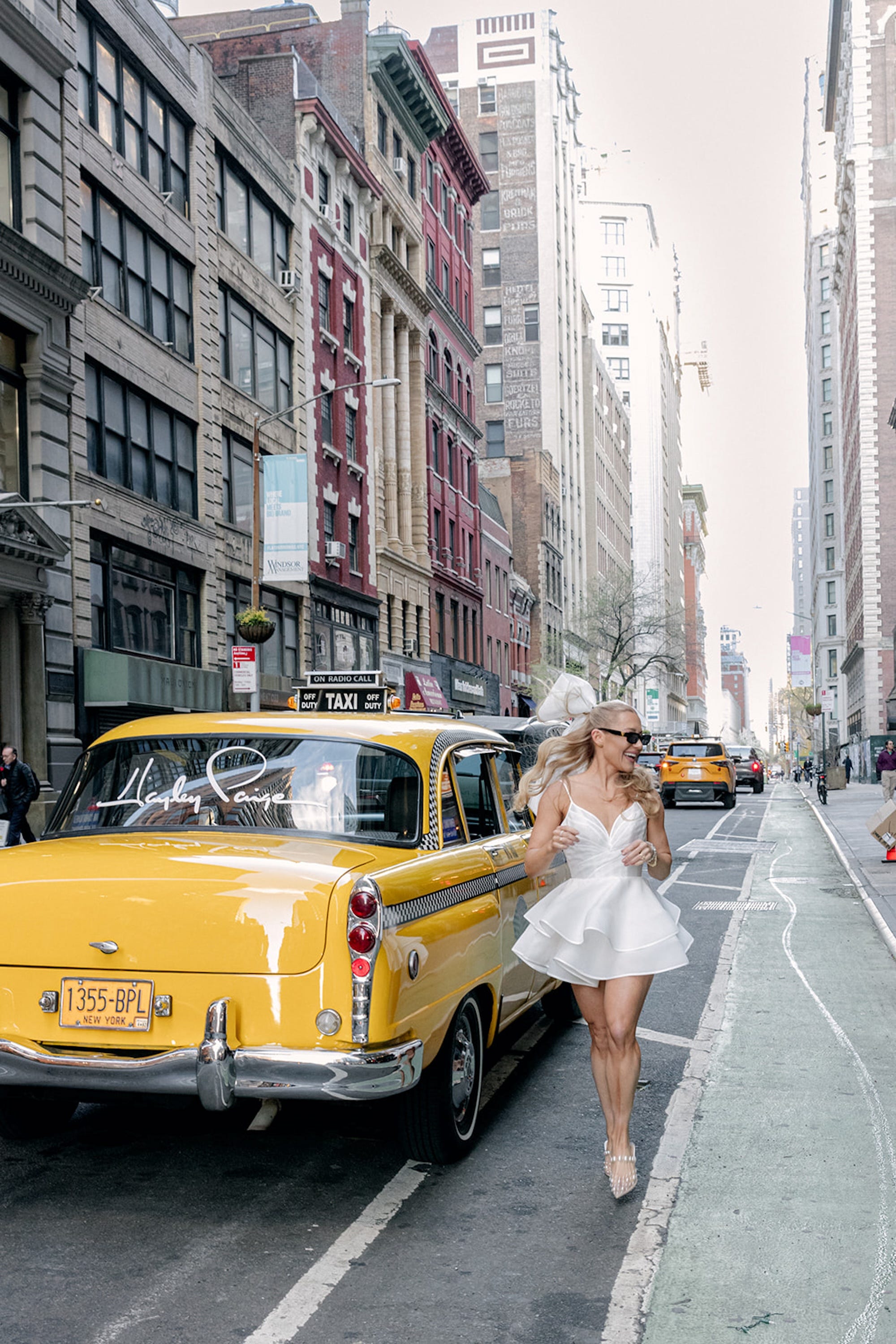 Hayley Paige skips next to a taxi with her name printed on it.