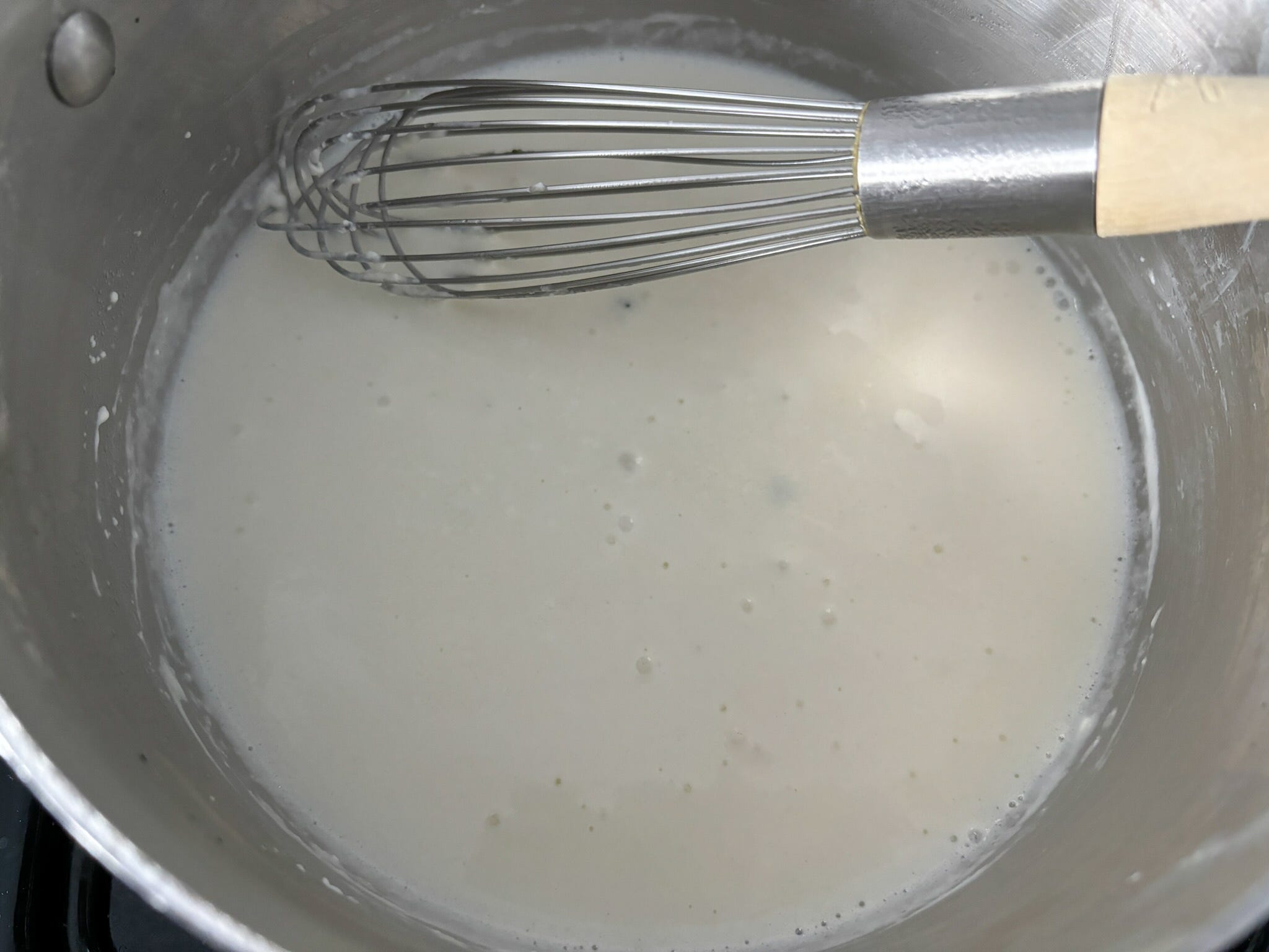 The pot of melted cream cheese, butter, and pasta water with the author's whisk in frame.