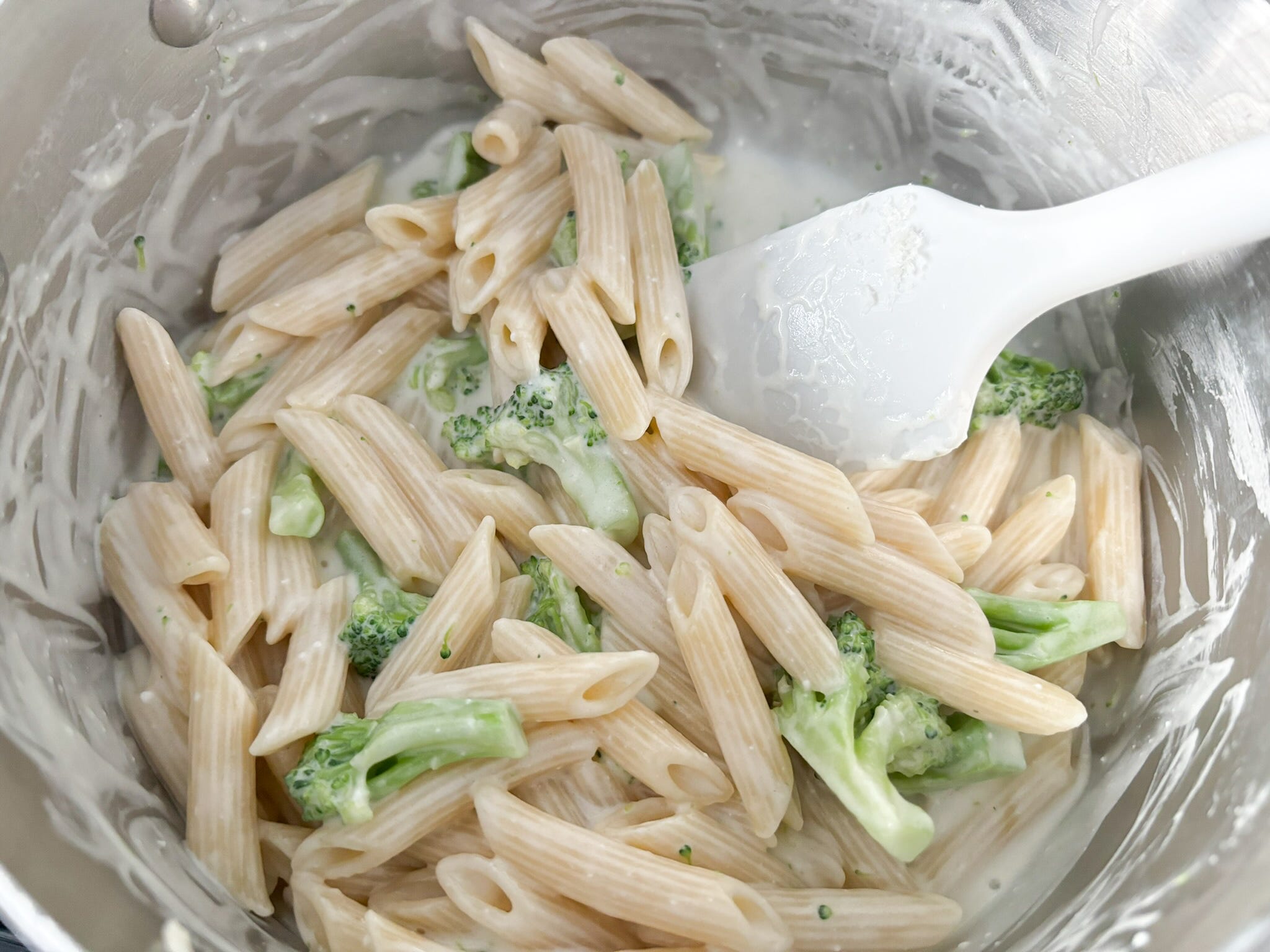 The pasta, broccoli, cheese, and sauce mixed together in the pot.