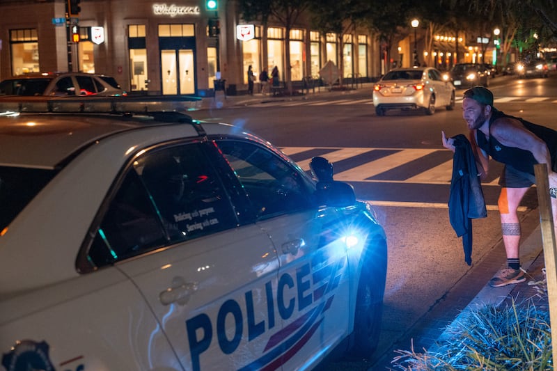 A protester flips off officers in a Metropolitan Police Department patrol car on August 13, 2025 in Washington, D.C.