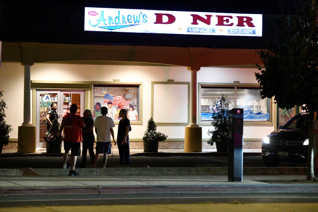 Photo of Andrew's Diner at night, with people standing outside and a police officer nearby.