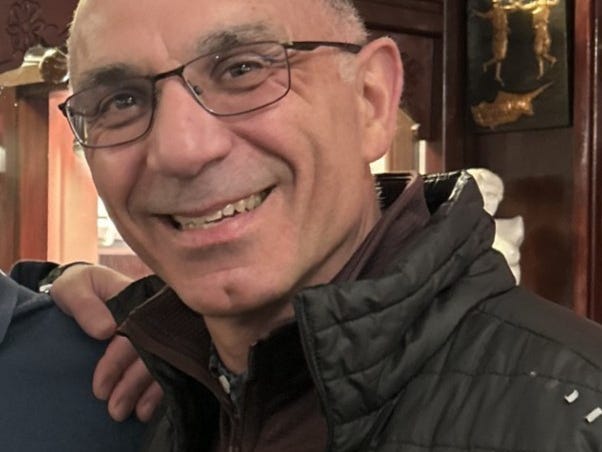 a bald man with glasses and a vest smiling