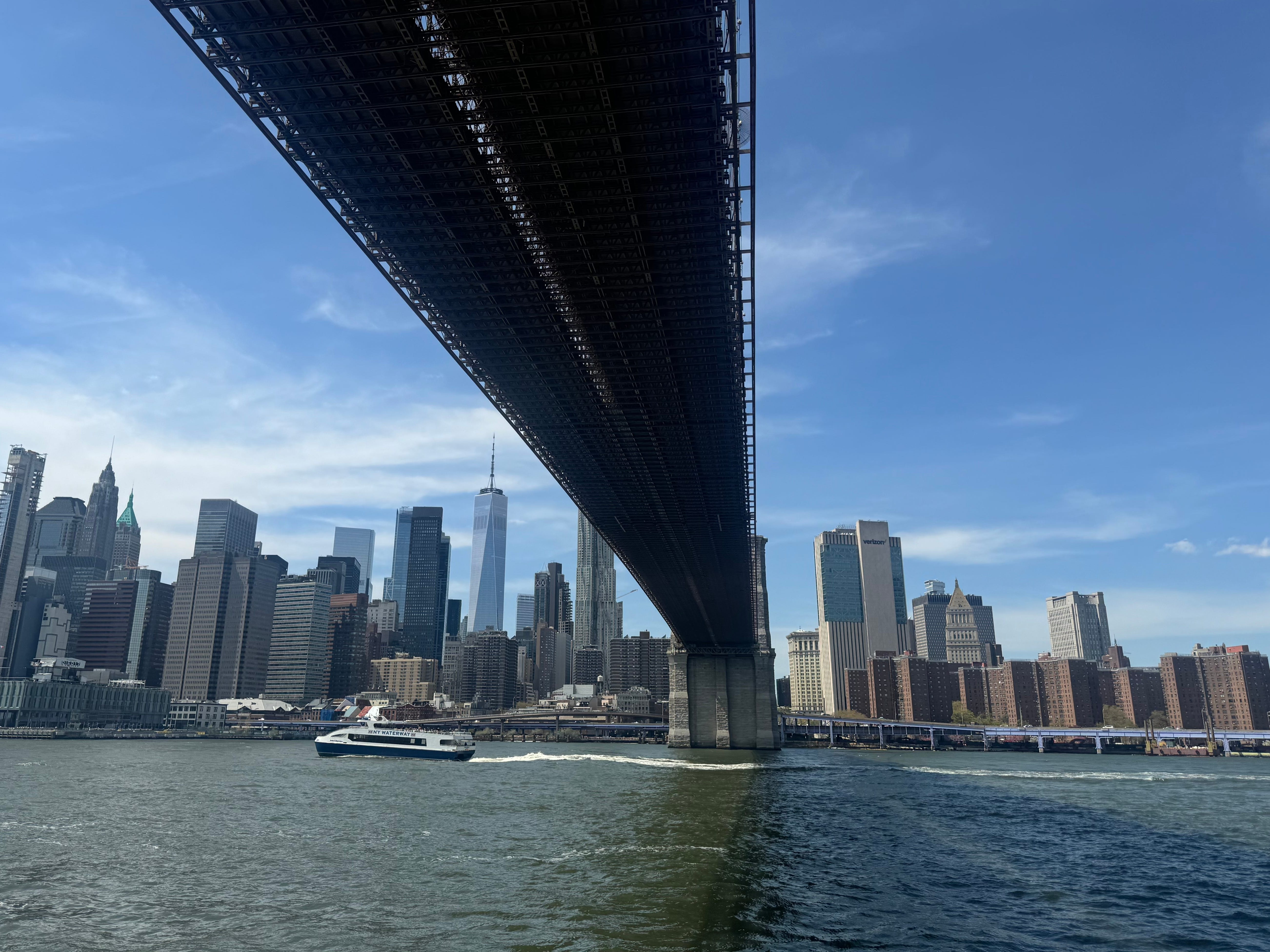 The underside of the Brooklyn Bridge, with the Manhattan skyline in the distance.