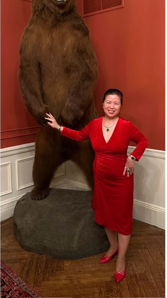 Woman in red dress standing next to a large taxidermied brown bear.