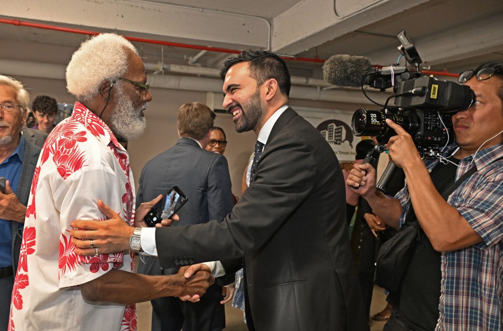 Zohran Mamdani shaking hands with a supporter at a community center.
