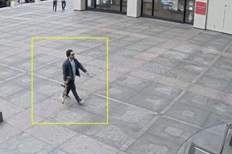 Surveillance image of Shane Devon Tamura carrying a rifle.