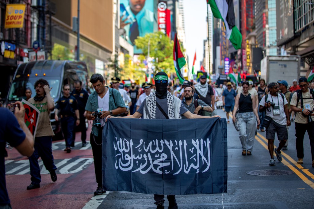 Person carrying a black flag with Arabic script at a protest.