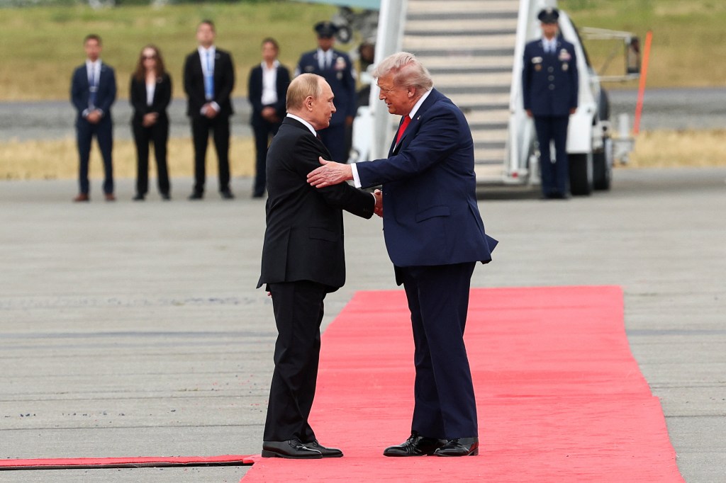 President Trump and President Putin shaking hands while Trump pats Putin's arm on a red carpet at Alaska summit on Aug. 15, 2025