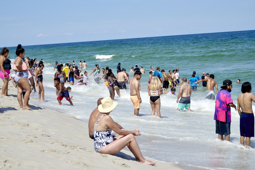 Crowded beach scene with people swimming and relaxing in the sand.
