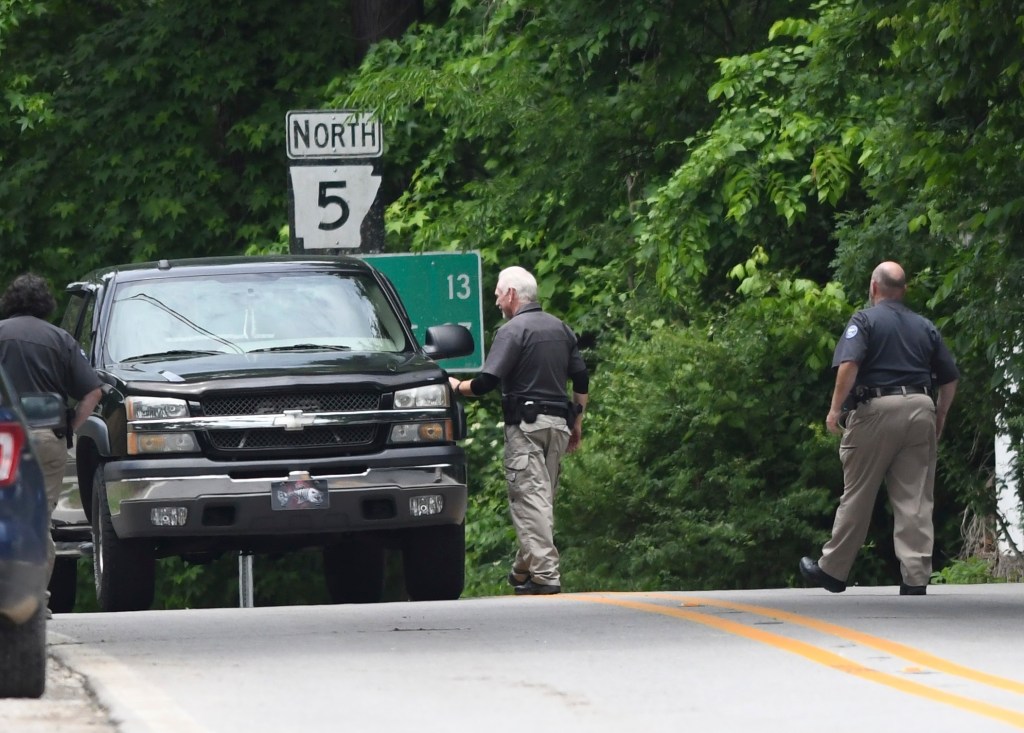 Police officers near a black truck on a roadside.