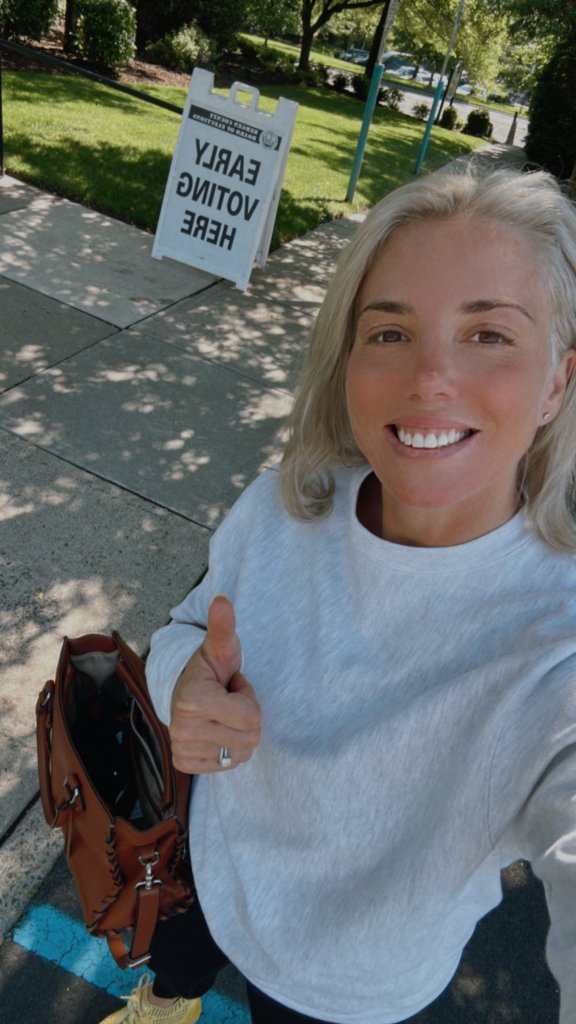Woman giving thumbs up near early voting sign.
