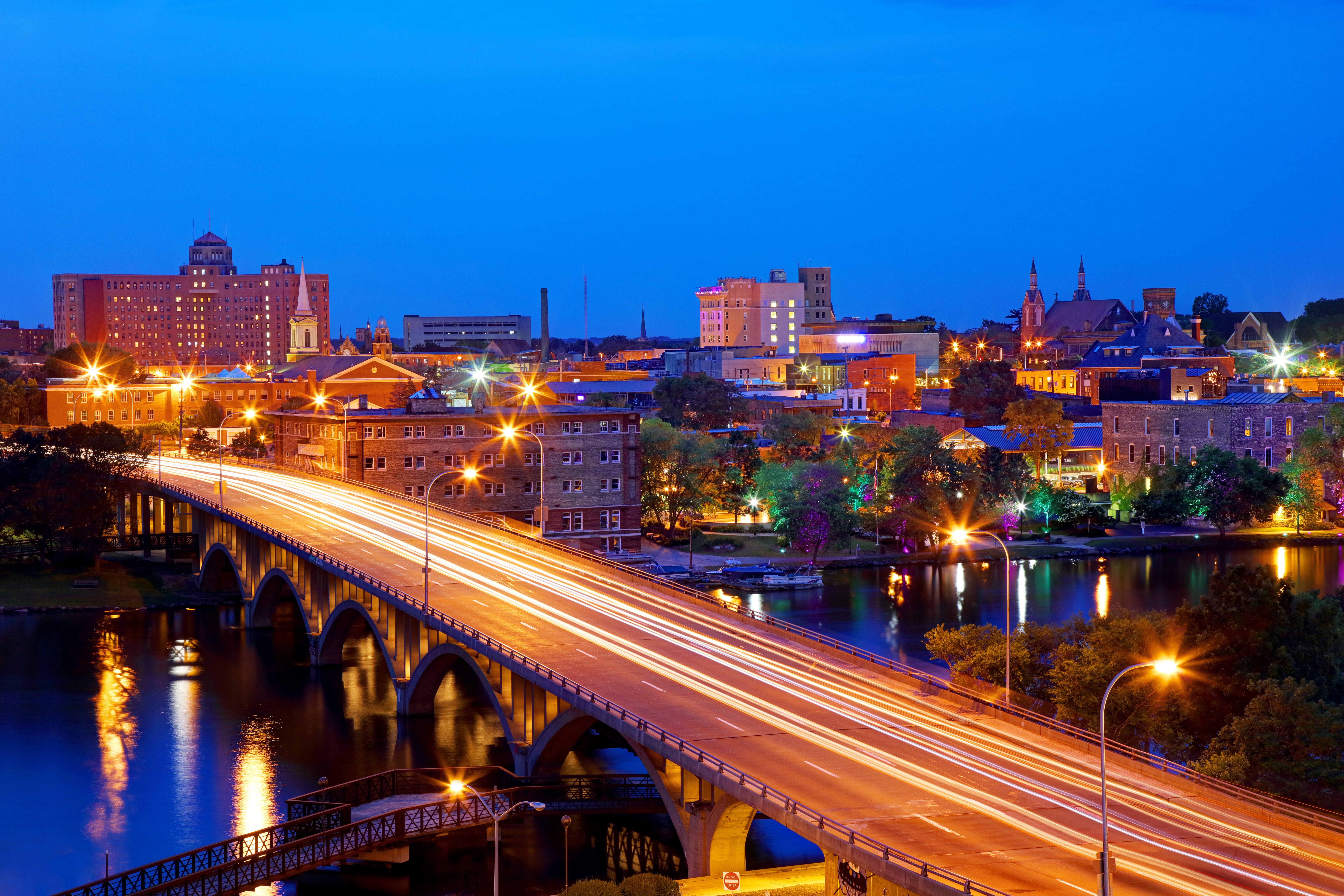 The small city skyline of Rockford, Illinois at dusk with traffic going over a bridge.