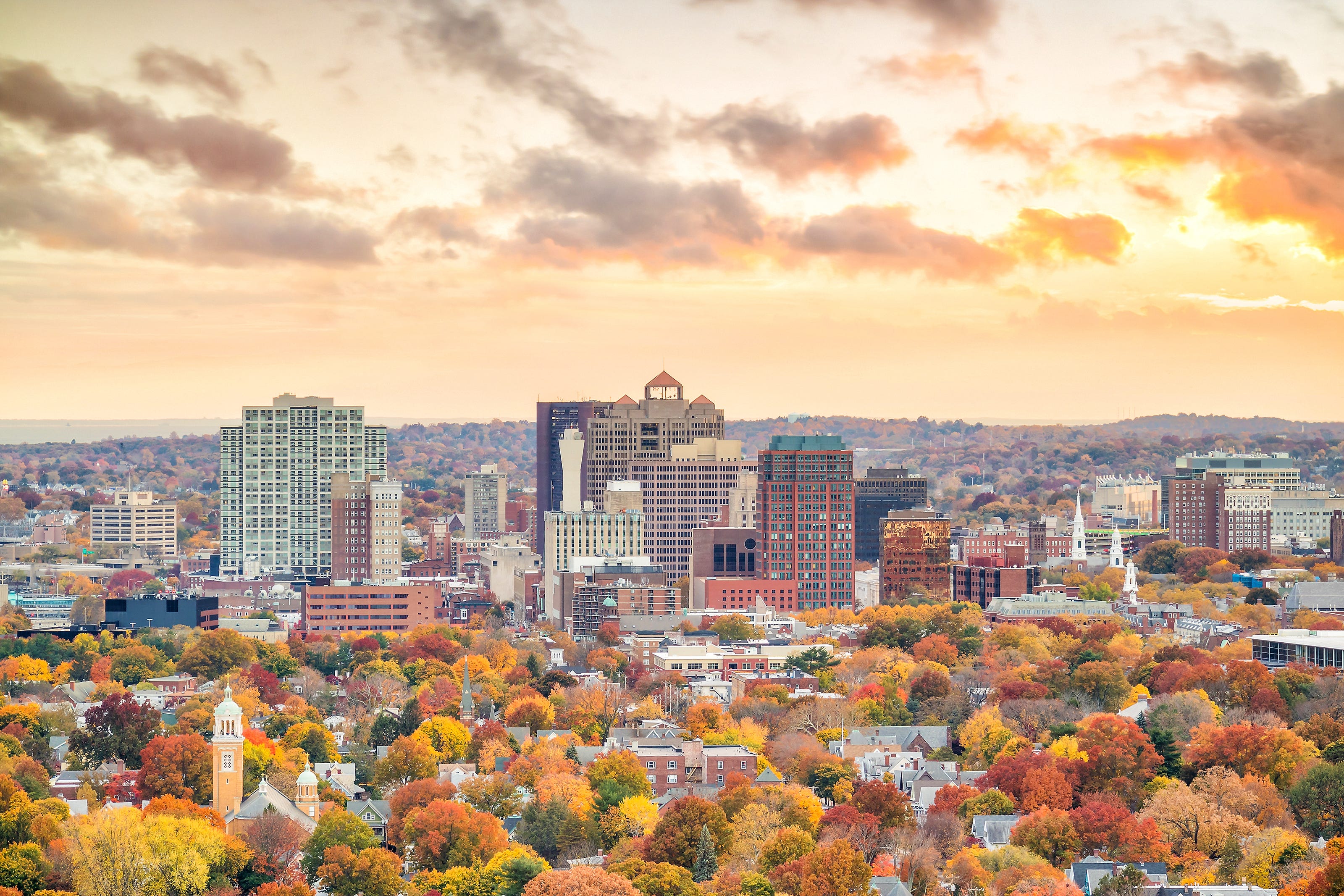 Downtown New Haven, Connecticut, during fall. The trees are varying shades of green, orange, yellow, and red. The sky has an orange tint, too.