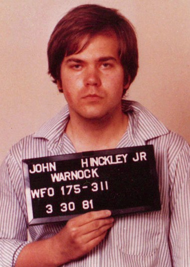 Mugshot of John Hinckley Jr. holding a prison identification plate.