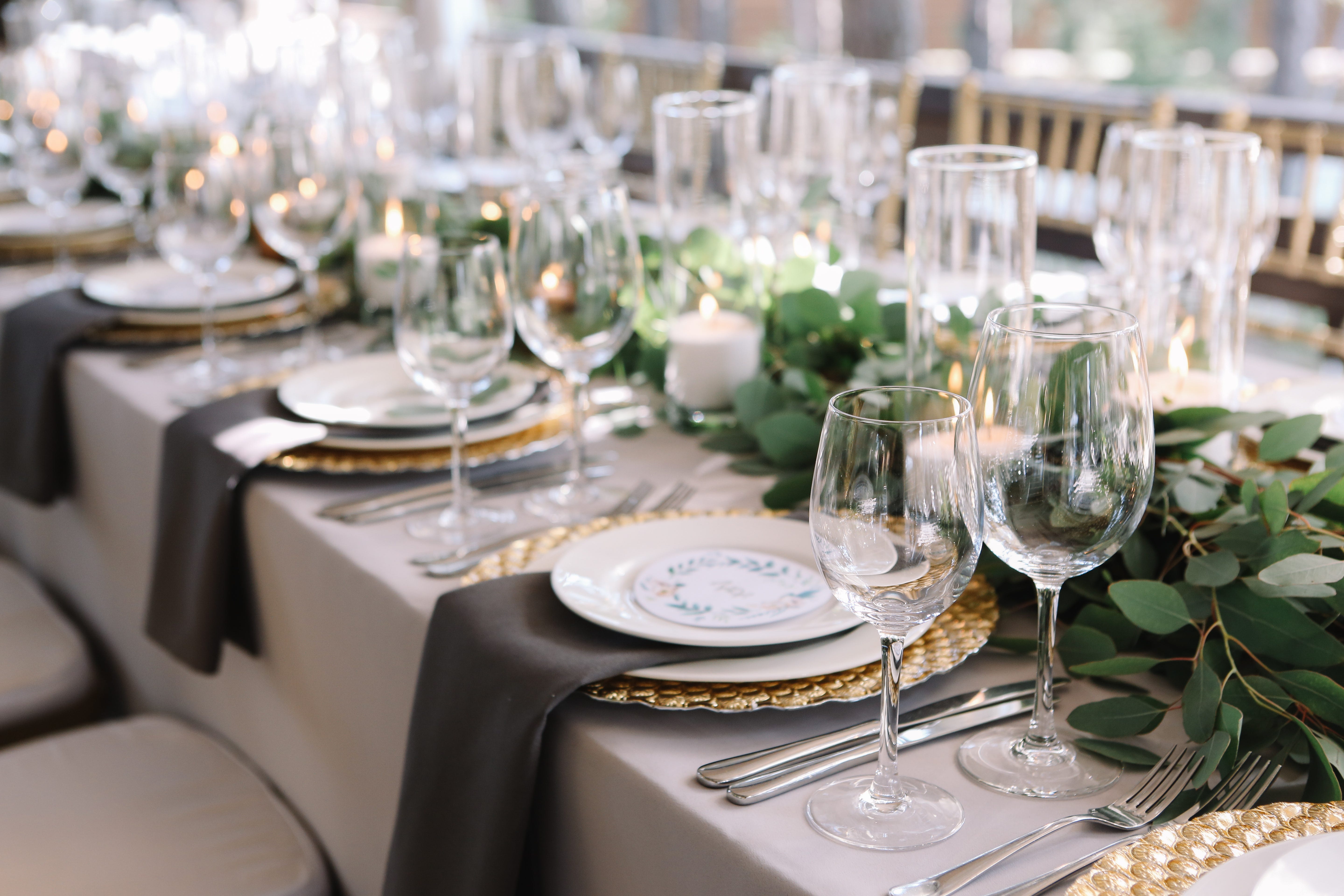 Place settings with gold chargers, wine glasses, water goblets, and draped napkins at wedding