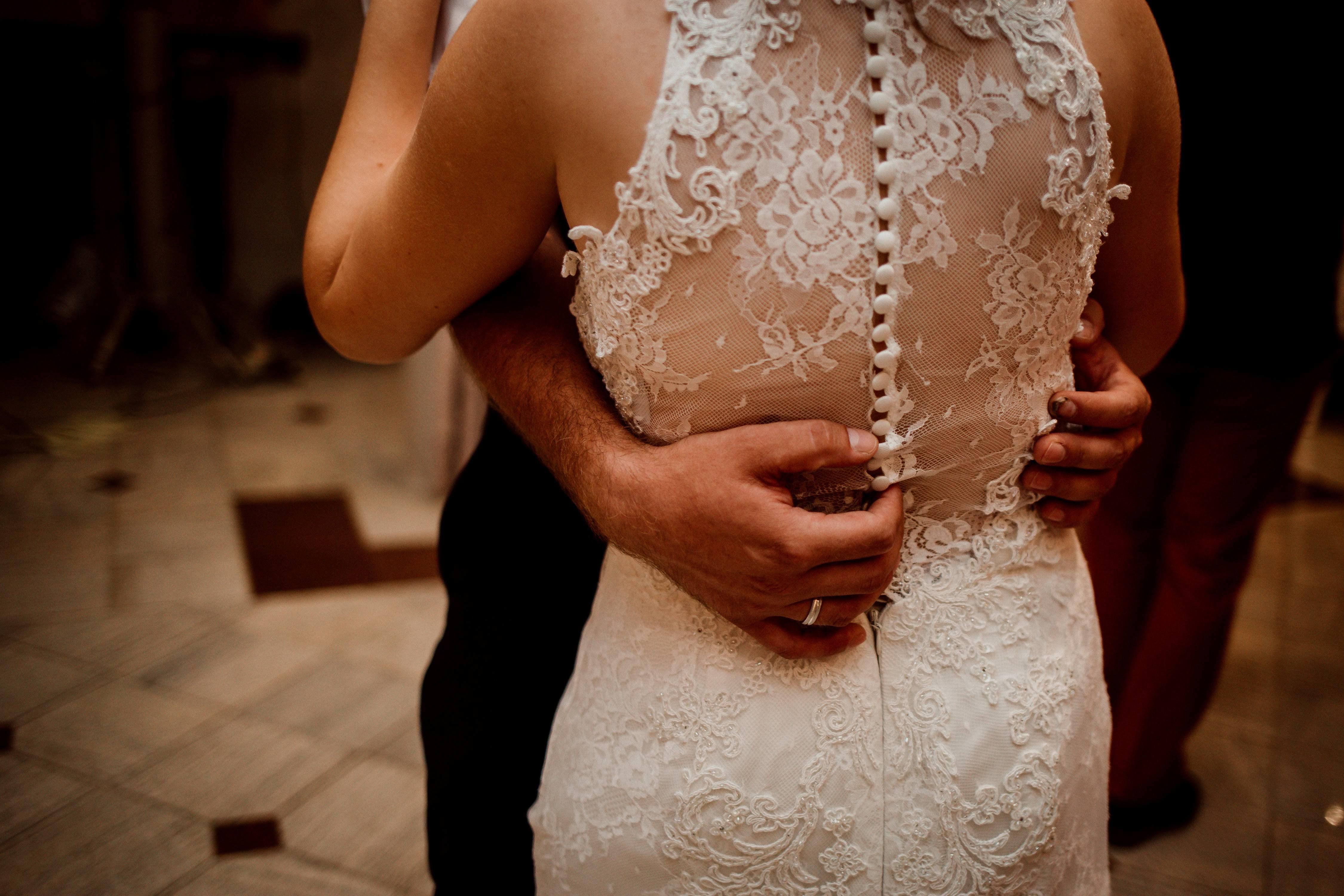 Hands holding back of person in wedding dress as they slow dance