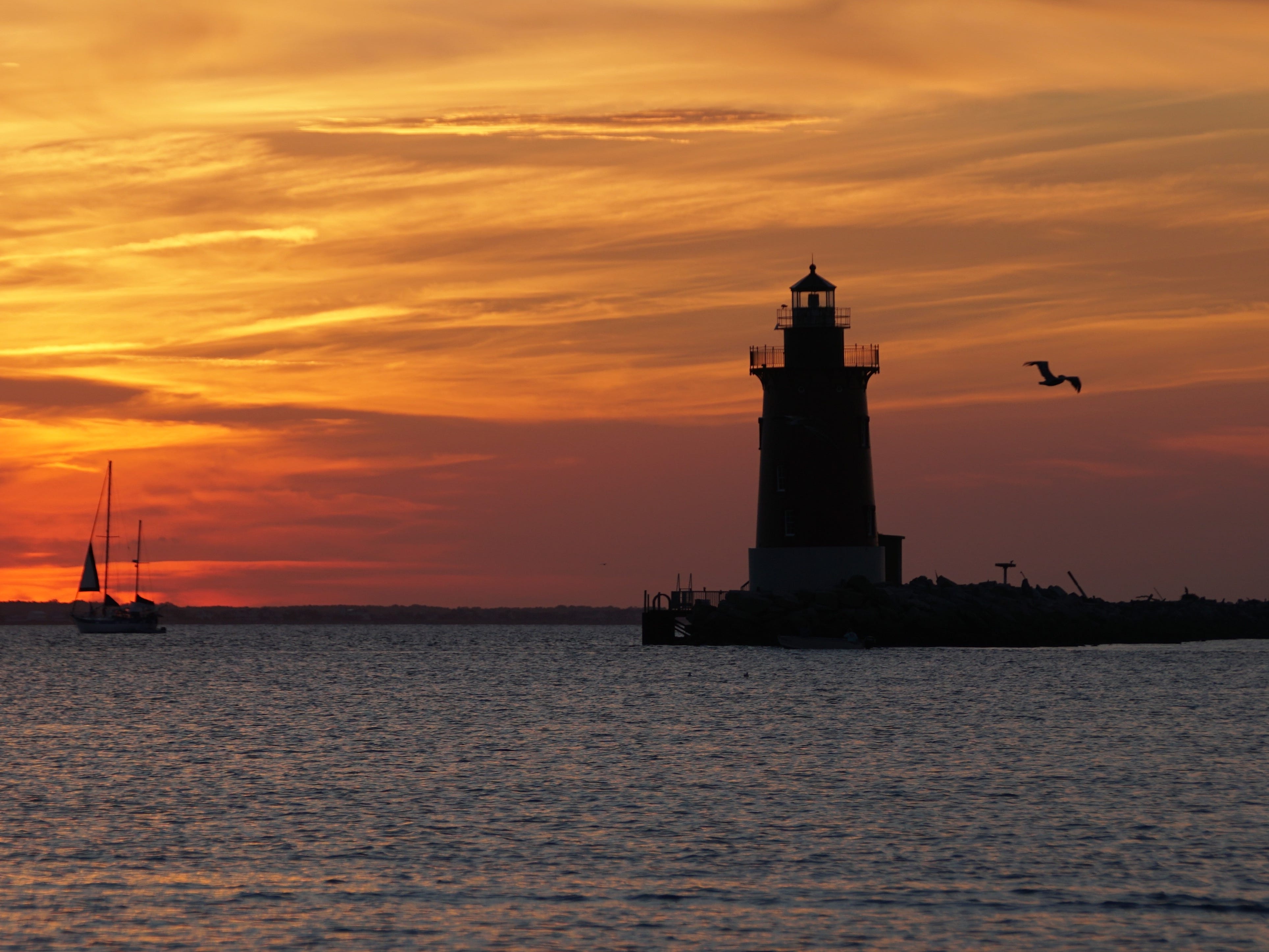 Silhouette of the lighthouse and a yacht during sunset near Cape Henlopen State Park.