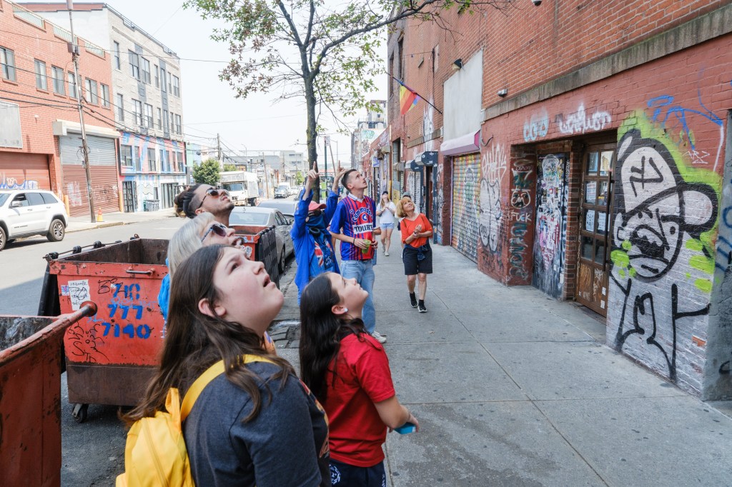 A group of people on a graffiti tour look up at street art.