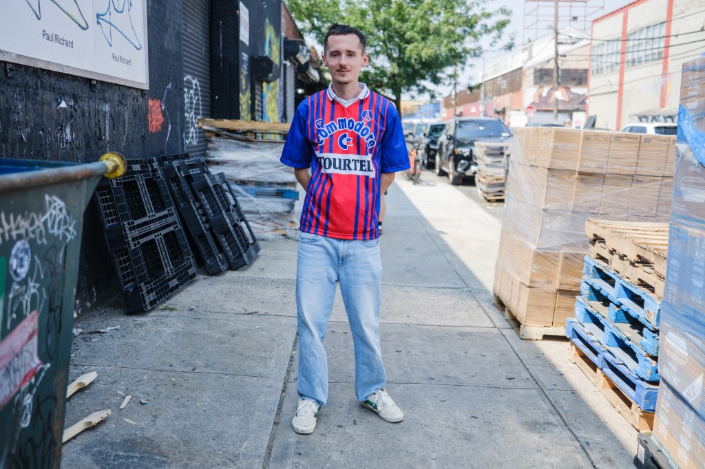 Man in soccer jersey standing on city sidewalk.