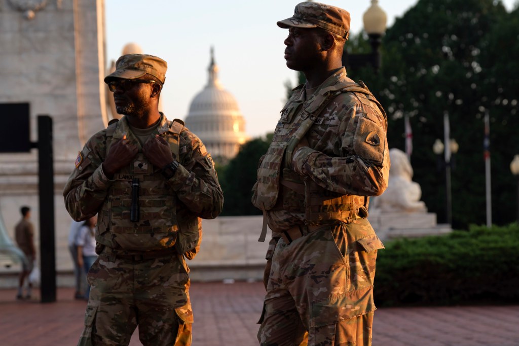 Two National Guard soldiers in camouflage uniforms stand outside Union Station in Washington, D.C., with the Capitol building in the background.