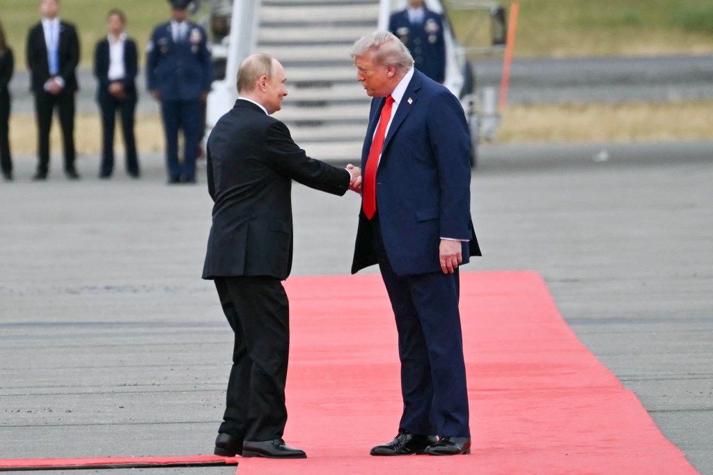 Donald Trump and Vladimir Putin shaking hands on a red carpet.