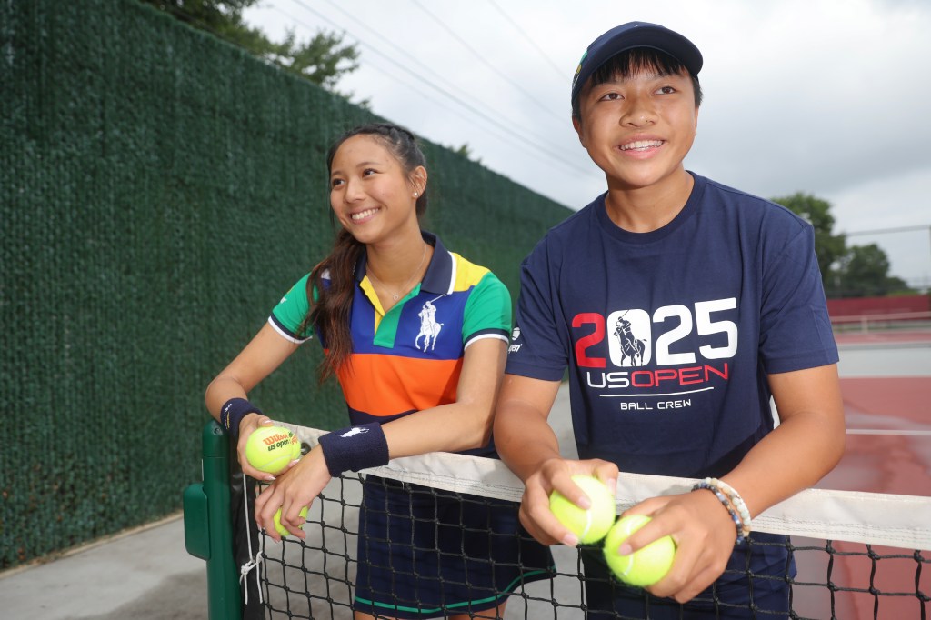 Two teenagers, a girl and a boy, pose for a portrait at a tennis court; they are holding tennis balls and wearing US Open ball crew shirts.