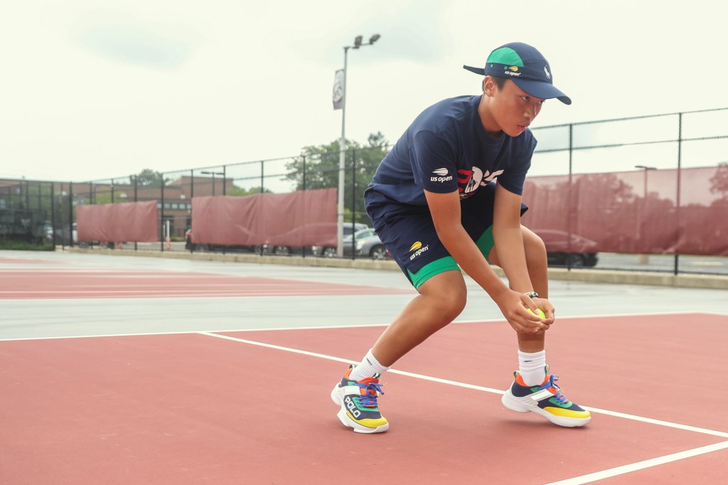 A teenage boy in US Open attire practices retrieving tennis balls on a court.