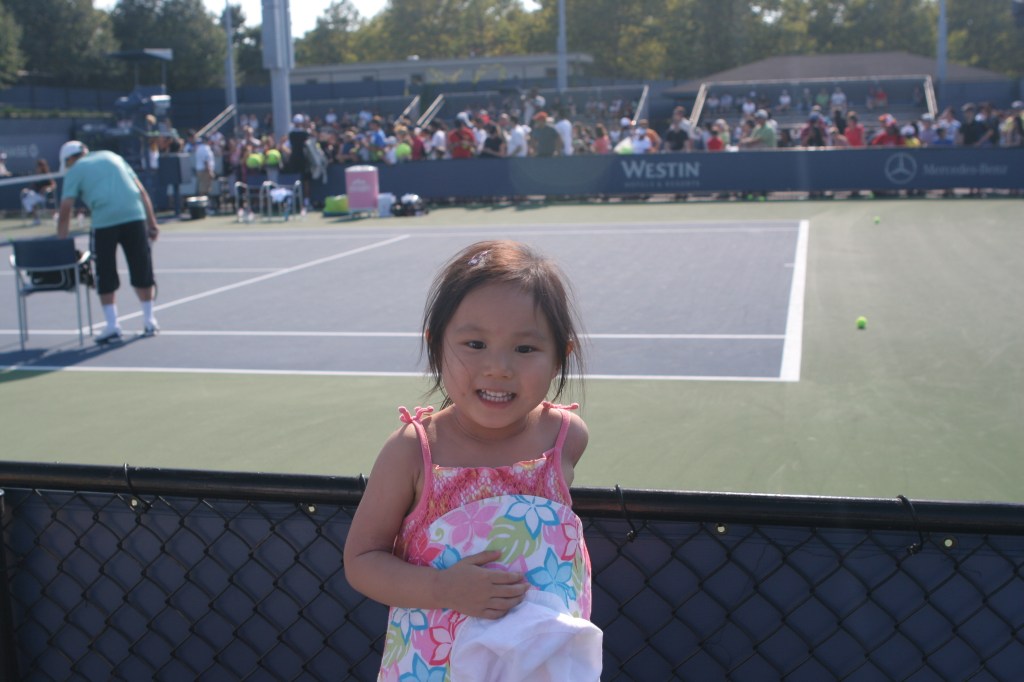 Young girl smiling at a tennis court.