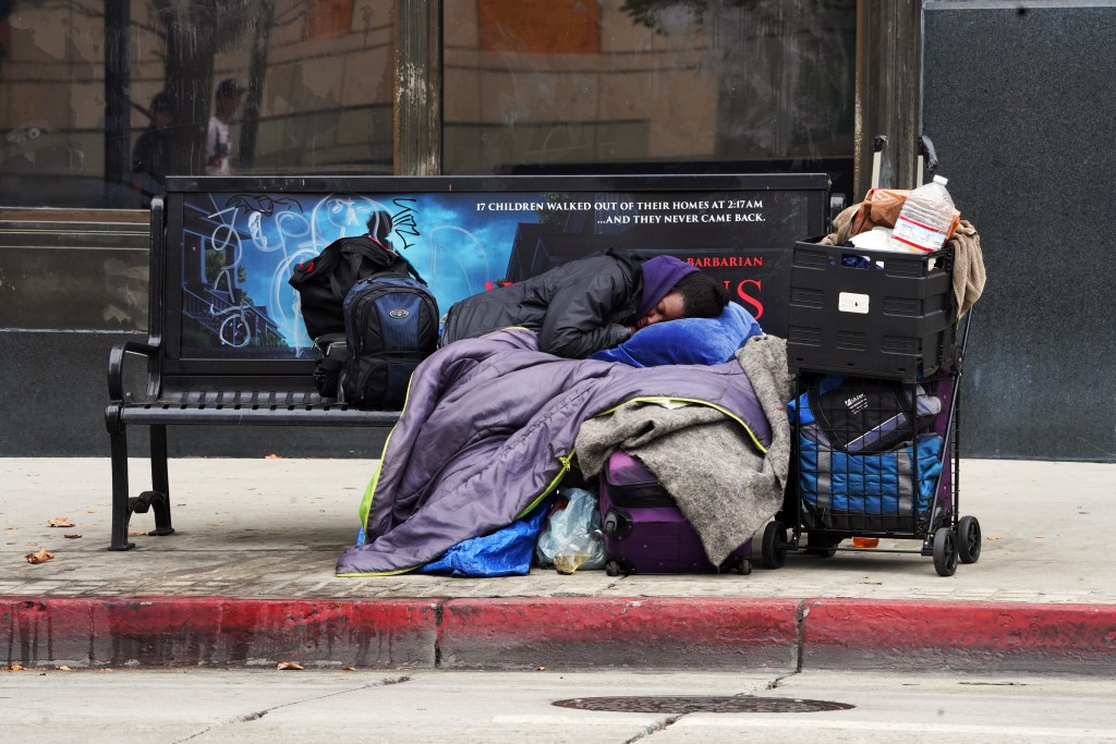 A homeless person sleeping on a bench at a bus stop in DTLA.