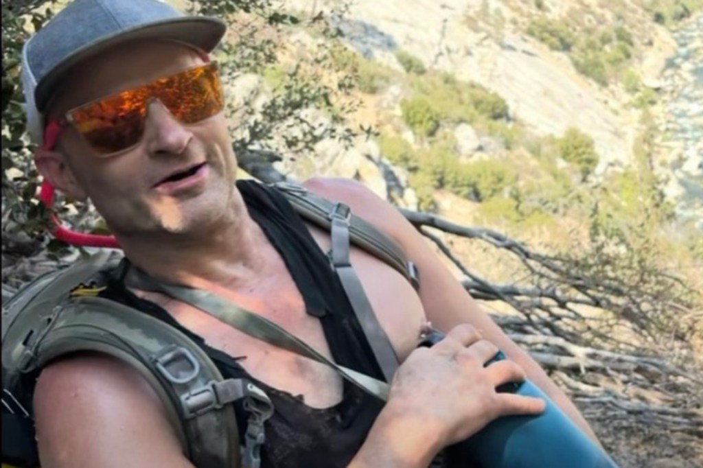 Man in sunglasses and backpack sits outdoors.