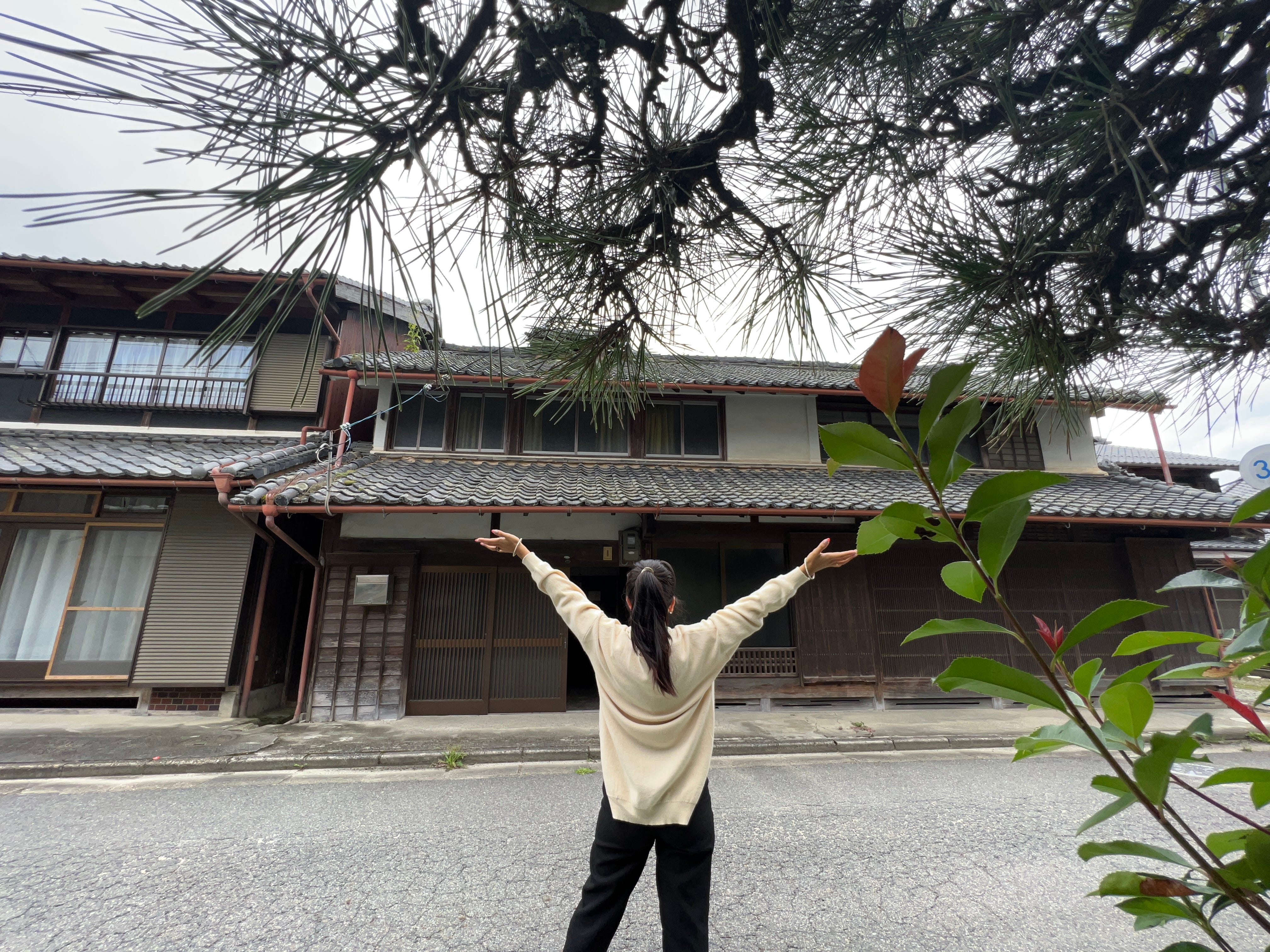 A woman standing in front of a traditional farmhouse in the Japanese countryside.