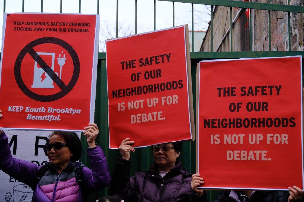 Protestors holding signs against dangerous battery charging stations in their neighborhood.