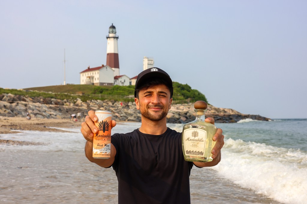 Man on beach holding Montaukila tequila and tequila soda, with lighthouse in background.