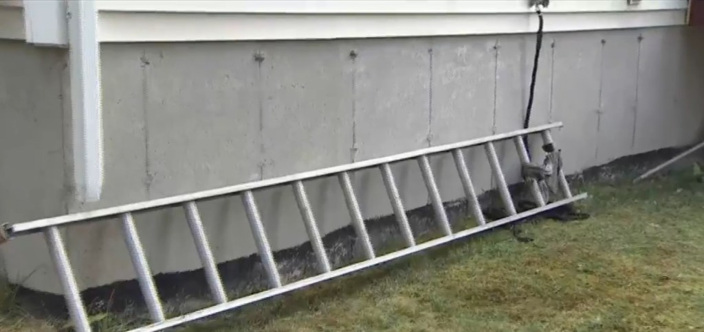 Aluminum ladder leaning against house foundation.